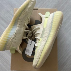 A pair of flax yeezy 350 sneakers, size 9.5m, priced at $265, placed atop their box on a grey floor.