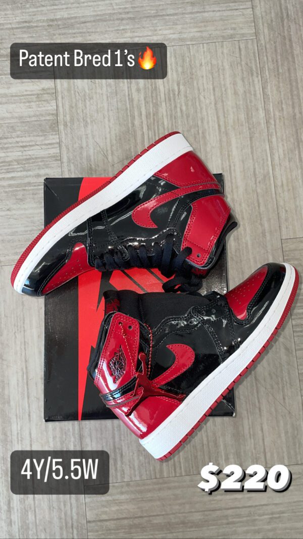 A pair of red and black Patent Bred 1's sneakers displayed on their box with a price tag of $220 shown on a wooden floor.