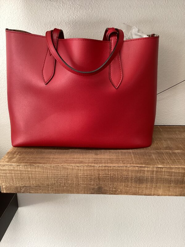 Burberry Red Reversible Tote on a wooden shelf against a white wall.