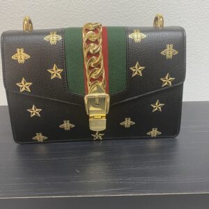 Black designer handbag with gold star embellishments, featuring a green and red striped center strap and a gold clasp.
