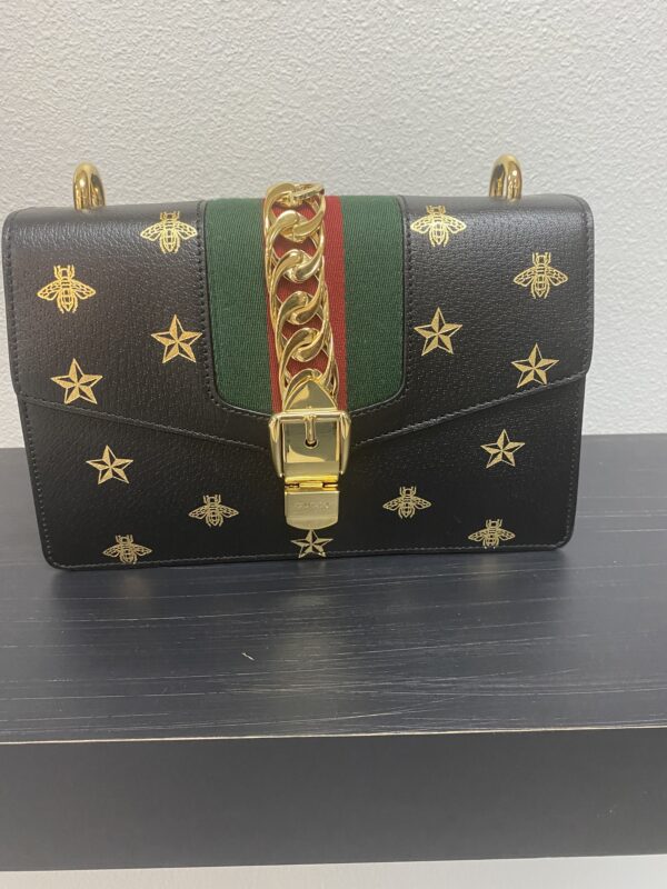 Black designer handbag with gold star embellishments, featuring a green and red striped center strap and a gold clasp.