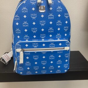 Blue mcm branded backpack with logo pattern, featuring a top handle, zippered compartments, and a price tag, displayed on a black shelf.