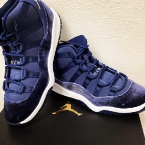 A pair of navy blue Jordan 11 Retro Marine Minuit sneakers displayed on a black surface with a gold jumpman logo visible.