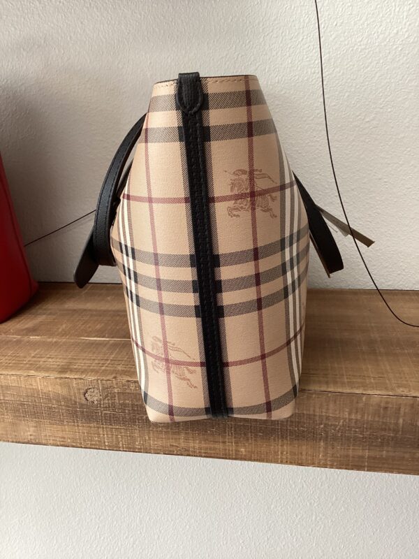 A beige checkered Burberry (Reversible) Tote with black leather straps, displayed on a wooden shelf.