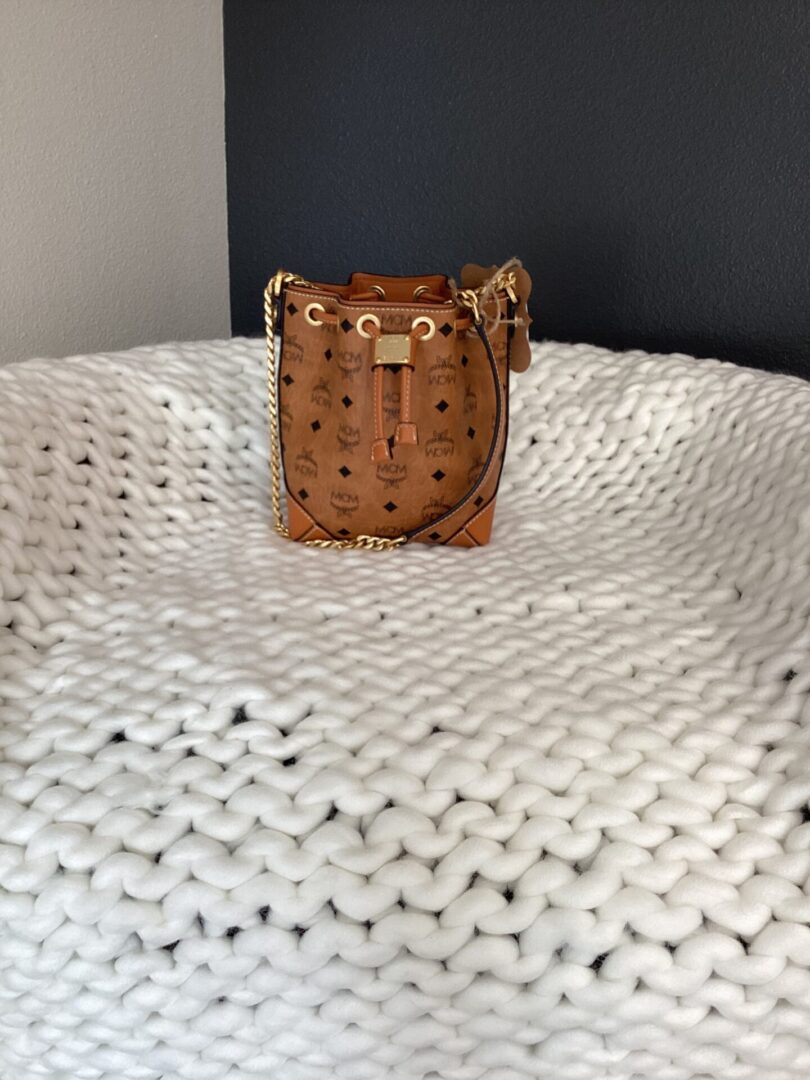 A small, MCM Bucket Bag with a patterned finish and gold hardware, resting on a textured white woven blanket.