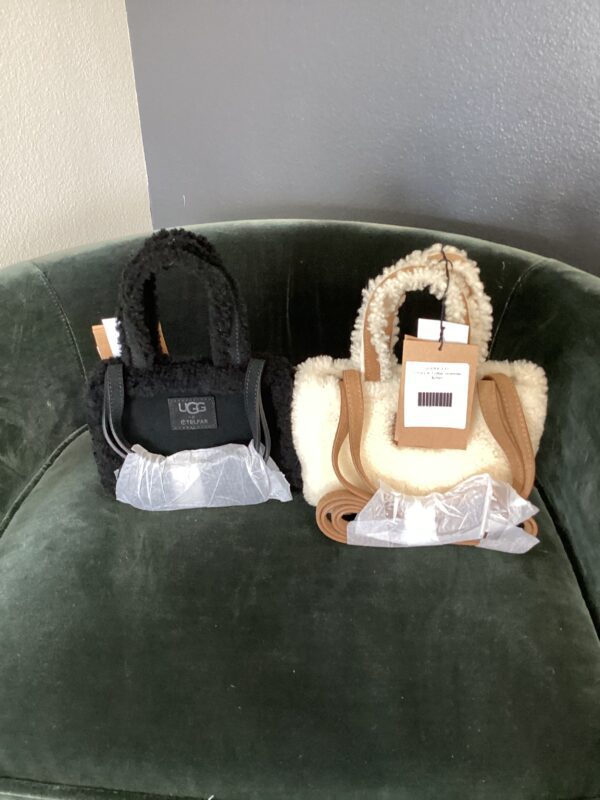 Two new UGG X Telfar bags with tags, one black and one beige, displayed on a green velvet chair.