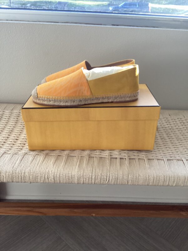 A pair of Fendi Yellow Espadrilles on a shoebox placed on a textured bench near a window.