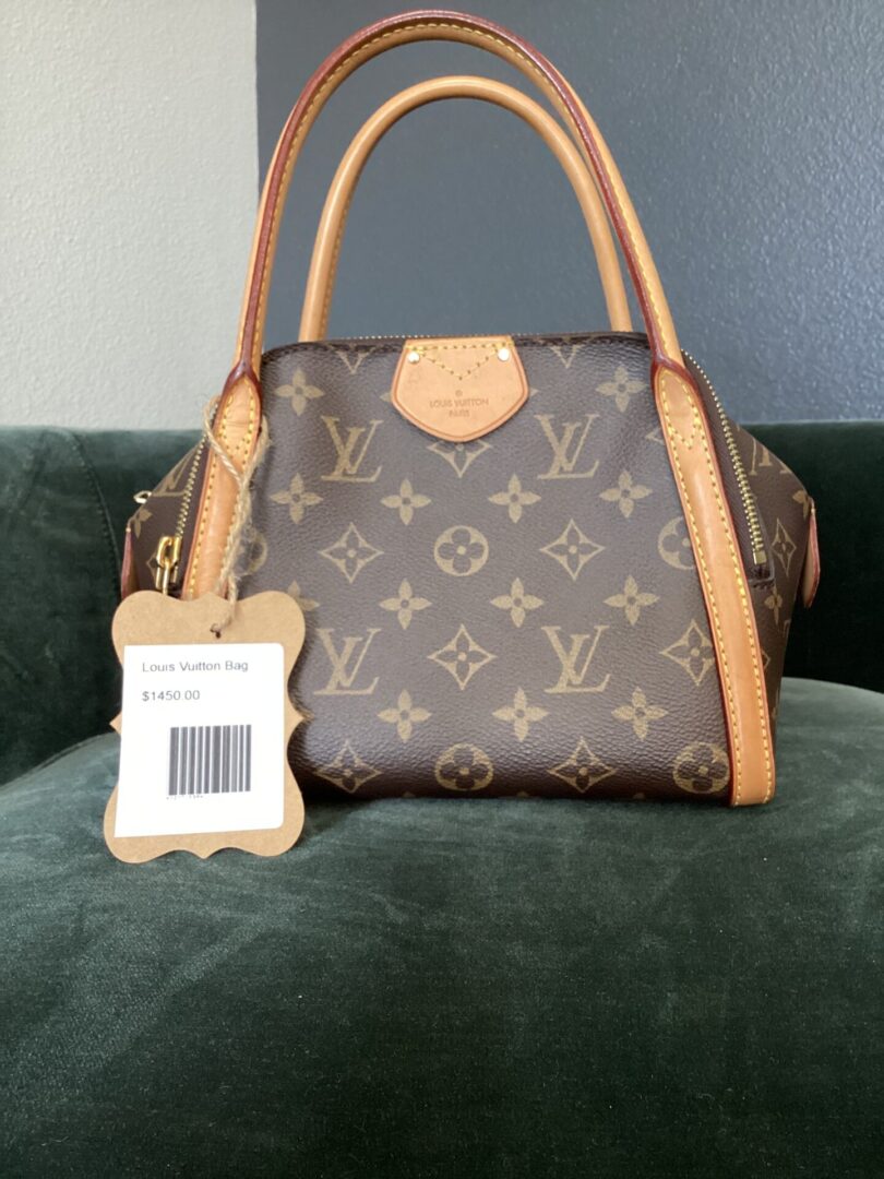 A Louis Vuitton Bag with a price tag of $1,450 placed on a green sofa. the bag features the iconic lv monogram print and tan leather trims.