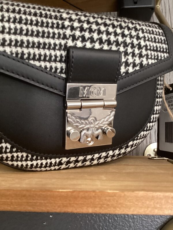 Black and white houndstooth MCM 2-Way Belt bag with a silver logo clasp on a wooden shelf.