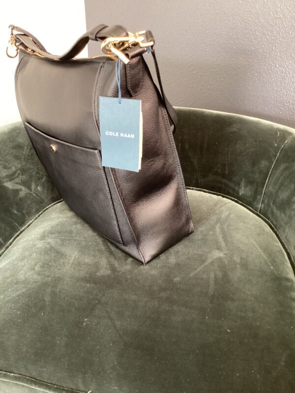 A new Cole Haan bag on a green velvet armchair.
