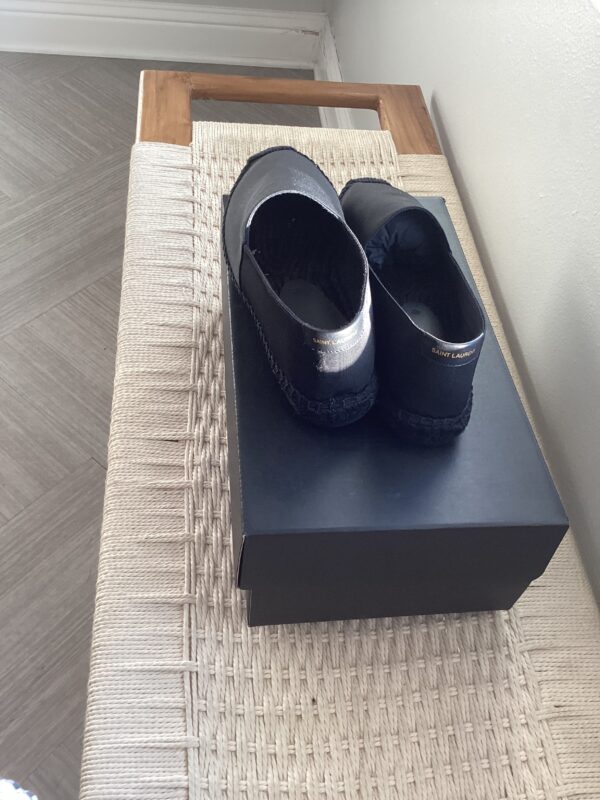 A pair of YSL Espadrilles placed neatly on a shoebox on a woven bench indoors.