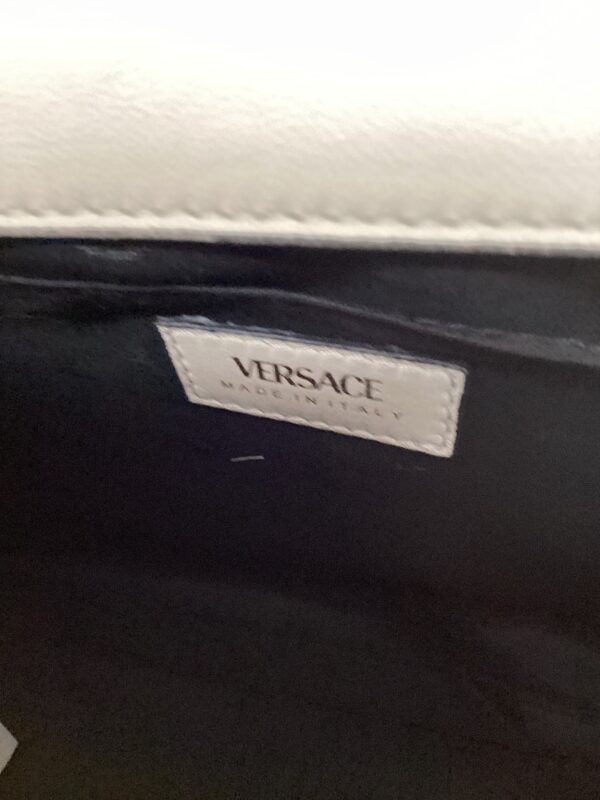 A close-up of a versace label with the text "made in italy" on a black leather background.