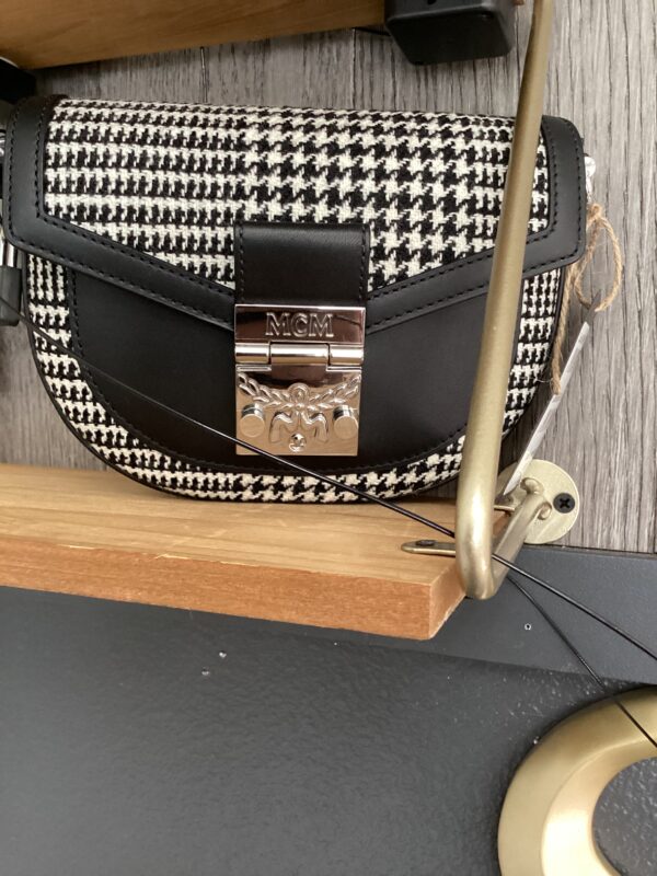 A black and white houndstooth patterned MCM 2-Way Belt bag with a metal clasp, resting on a wooden surface.