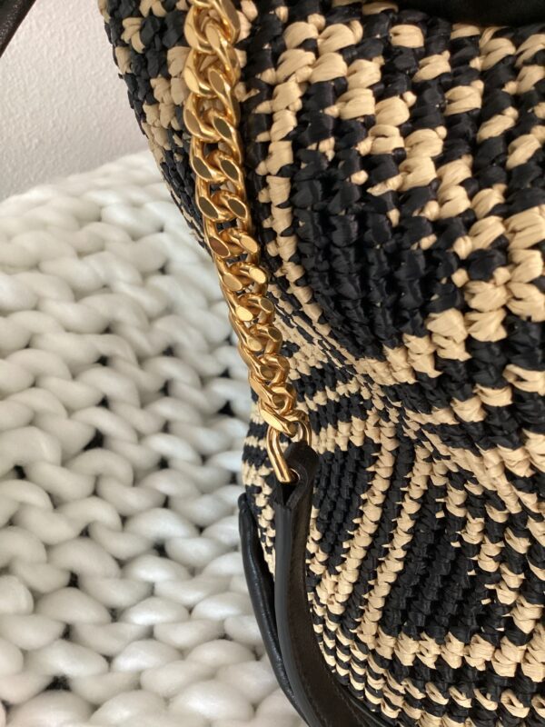 Close-up of a YSL Bucket Bag with a gold chain handle, resting against a white textured cushion.