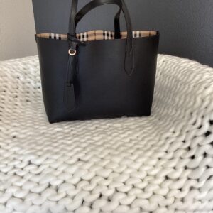 Burberry (Reversible) tote bag with plaid trim on a textured white blanket.