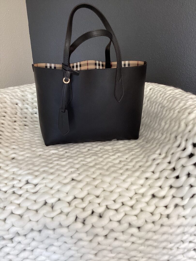 Burberry (Reversible) tote bag with plaid trim on a textured white blanket.