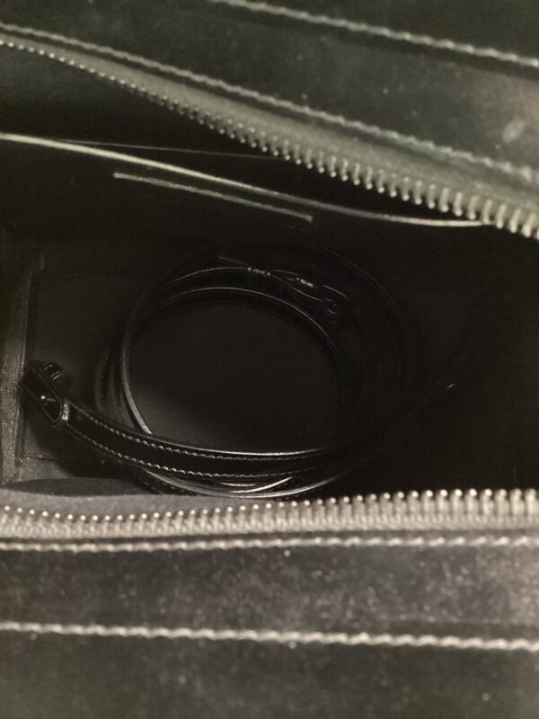 A black leather belt coiled inside a YSL Uptown Bag with visible textures of the suitcase fabric.