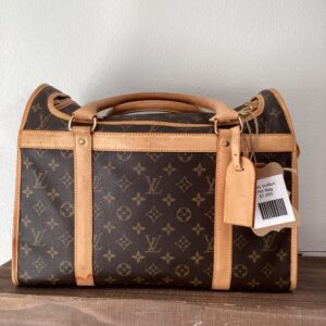 A Louis Vuitton Pet Travel Bag with the iconic monogram design placed on a wooden shelf, featuring tan leather accents and a barcode tag attached.