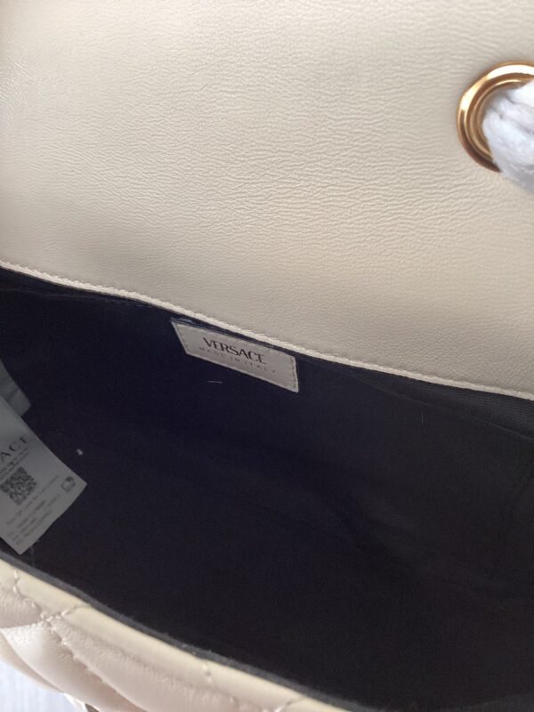 Close-up of an open white leather bag revealing a black interior with a metallic "versace" label.