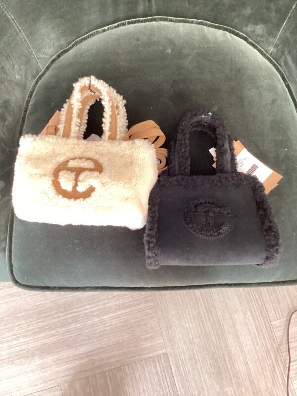 Two plush UGG X Telfar bags, one beige and one black, placed on a green velvet chair.