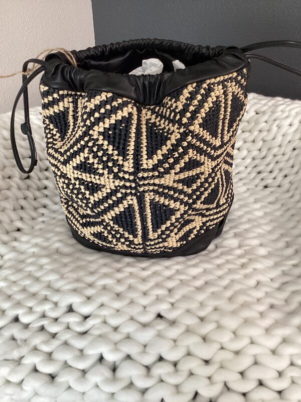 A YSL bucket bag with a geometric black and white pattern, placed on a textured white rug.
