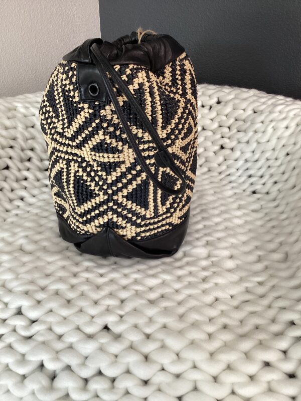 A YSL Bucket Bag on a white textured blanket. the bag features black and beige zigzag designs with leather accents.