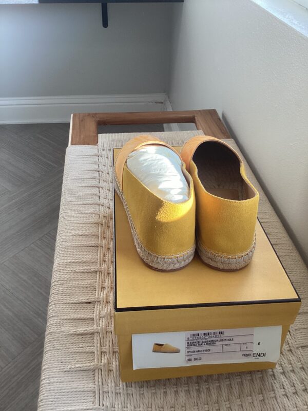 A pair of Fendi Yellow Espadrilles placed on a shoebox on a woven mat near a window.