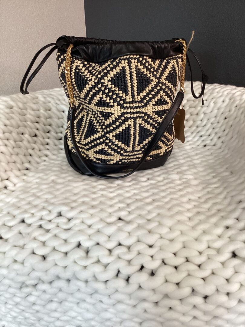 A YSL Bucket Bag with geometric designs, sitting on a textured white surface.