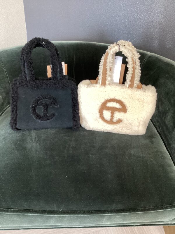 Two small UGG X Telfar bags, one black and one white, with circular logos, displayed on a green velvet chair.
