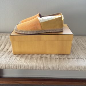 A pair of Fendi Yellow Espadrilles on a shoebox, placed on a textured bench near a window.