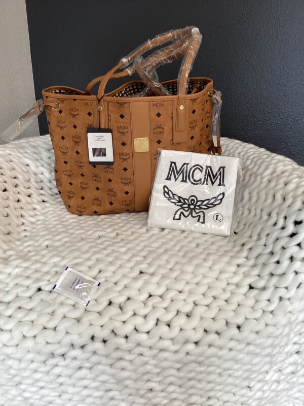 Two MCM Shopper bags, one large and one small, displayed on a textured white throw; price tags and packaging visible.