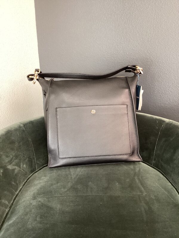 A black Cole Hana shoulder bag with a golden clasp on a dark green velvet chair.