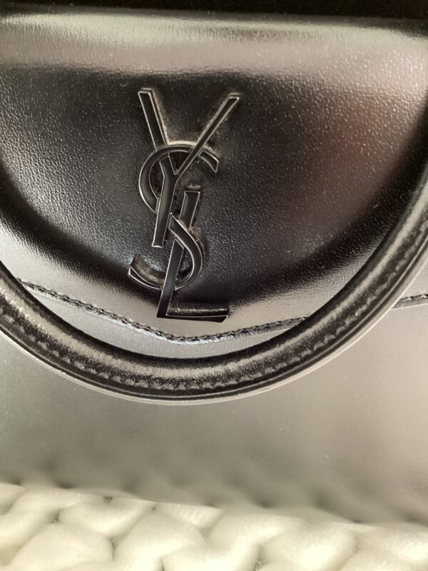 Close-up of a black leather YSL Uptown Bag with a prominent silver YSL logo on the clasp.