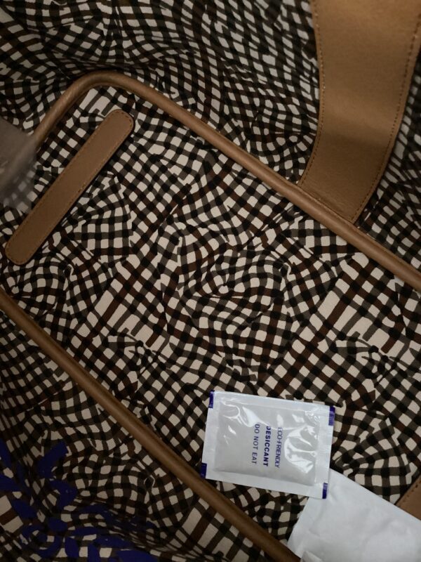 A close-up view of an MCM Shopper with a geometric pattern, featuring a visible handle and a white label reading "wet wipes.