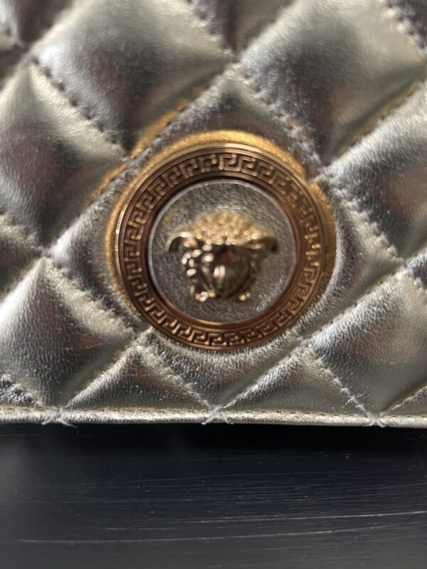 Close-up of a metallic gold button on a VERSACE Gold Bag, featuring a bee design and ornate pattern.