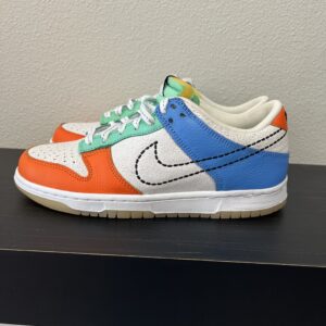 A colorful sneaker with orange, blue, and white panels and green laces on a simple black shelf.