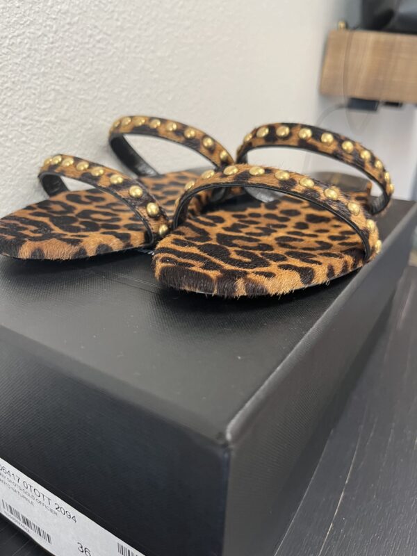 A pair of YSL Kiki Stud Sandals with leopard print, resting on a shoebox in an indoor setting.