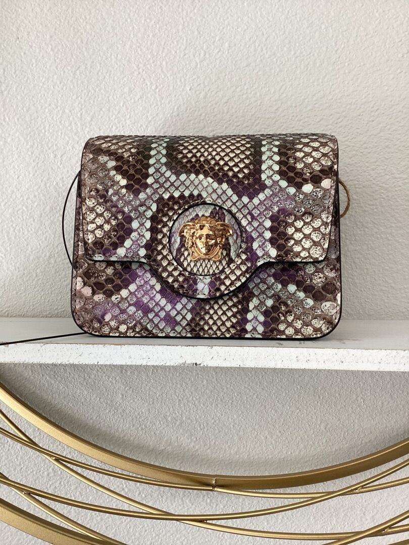 A YSL Bucket Bag with a lion head clasp, resting on a white shelf against a textured wall.