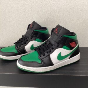 A pair of black and green Pre-owned Jordan 1 Mids sneakers with white nike swoosh logos displayed on a black shelf.