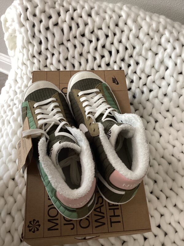 A pair of new Nike Dunk Low Retro green and white sneakers with tags, displayed on their box atop a white knitted blanket.