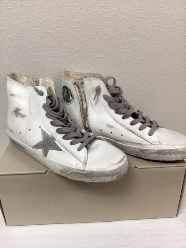 A pair of worn white high-top sneakers with a star design and side zippers, displayed against a plain background on top of a Burberry Bucket Bag.