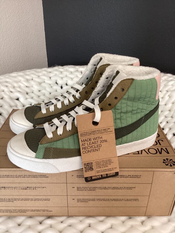 A pair of Nike Dunk Low Retro sneakers with green, beige, and brown panels, featuring a fleece lining and an eco-friendly tag, displayed on a shoebox.