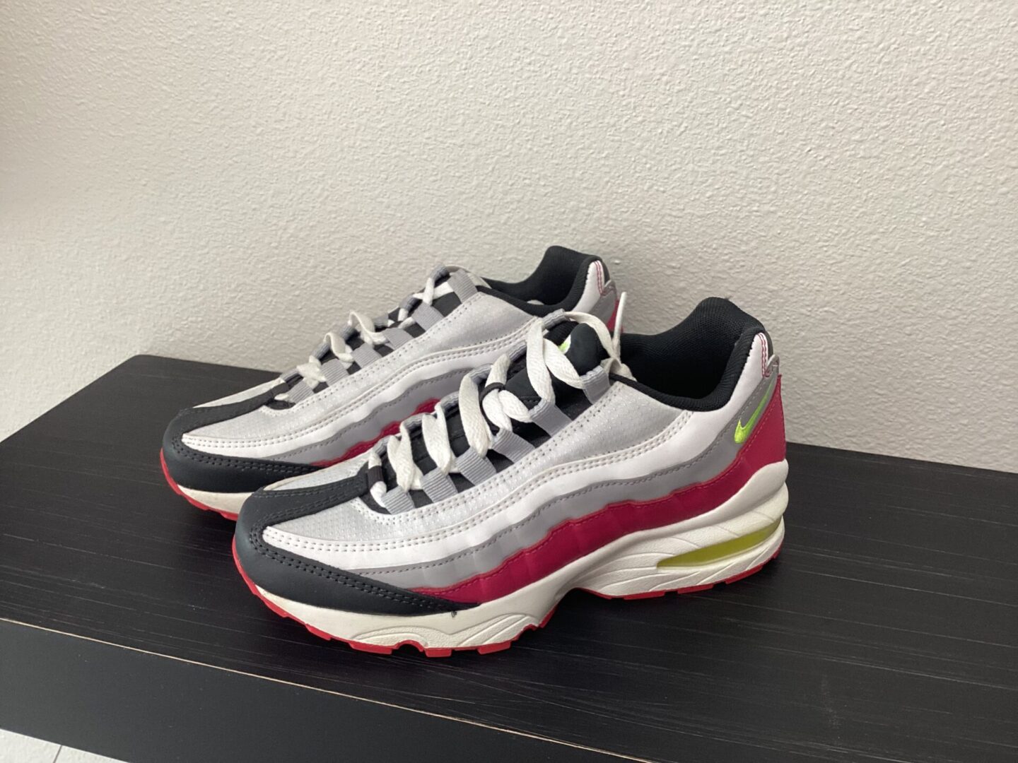 A pair of Pre-Owned NIKE-Airmax 95 with gray, white, and maroon accents on a black shelf against a white wall.