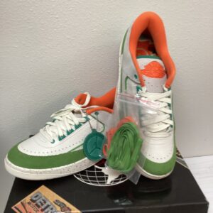 A pair of Jordan 2 Retro Low sneakers in green and white with additional laces attached, displayed on a black pedestal.