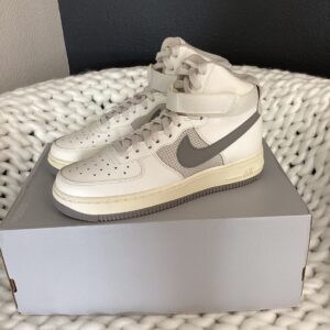 A pair of white Nike Dunk Low Retro sneakers displayed on their original box, set against a grey and white woven background.