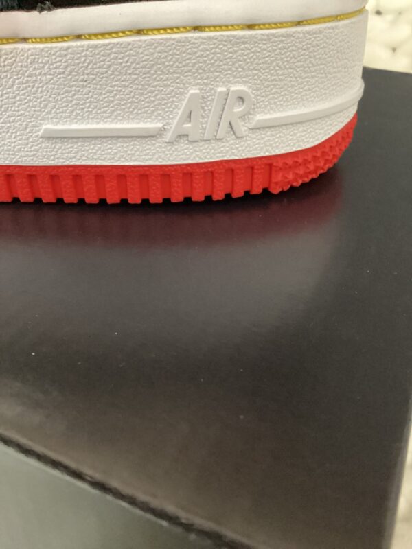 Close-up of a Air Force 1 Low shoe with a white "Air" logo on a grey band above a red rubber sole, displayed on a black surface.