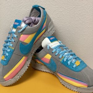 A Burberry Bucket Bag with grey uppers, pastel rainbow accents, and light blue laces displayed against a yellow background.