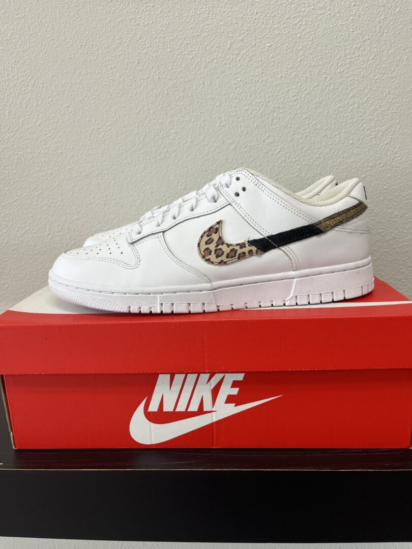 White NIKE-Dunk Low White/Multi Animal sneaker with leopard print detail on the swoosh logo, displayed on top of a red nike shoebox.