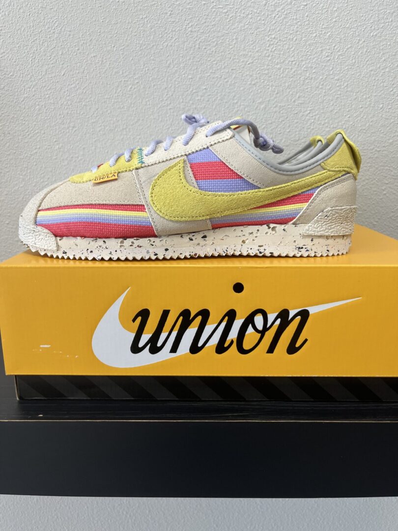 A Nike-Cortez UNION Lemon Frost with yellow and pastel stripes displayed on a shoebox.