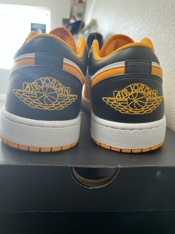 Rear view of two Jordan 1 Low Taxi/Black/White sneakers with the logo embroidered on the back, placed on a shoebox.